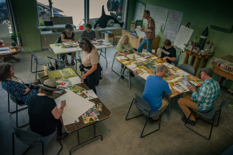 Birds-eye-view of artists gathered around tables constructing collages