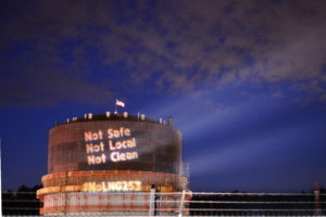 Text reading "Not Safe, Not Local, Not Clean" projected on the side of large oil tank in the Port of Tacoma