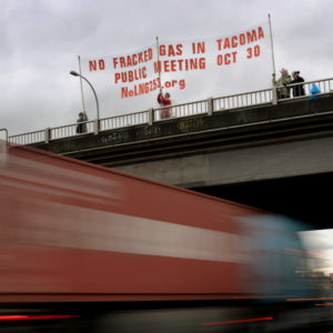 People stand on highway overpass holding a banner that reads "no fracked gas in Tacoma, public meeting Oct 30, NoLNG253.org"